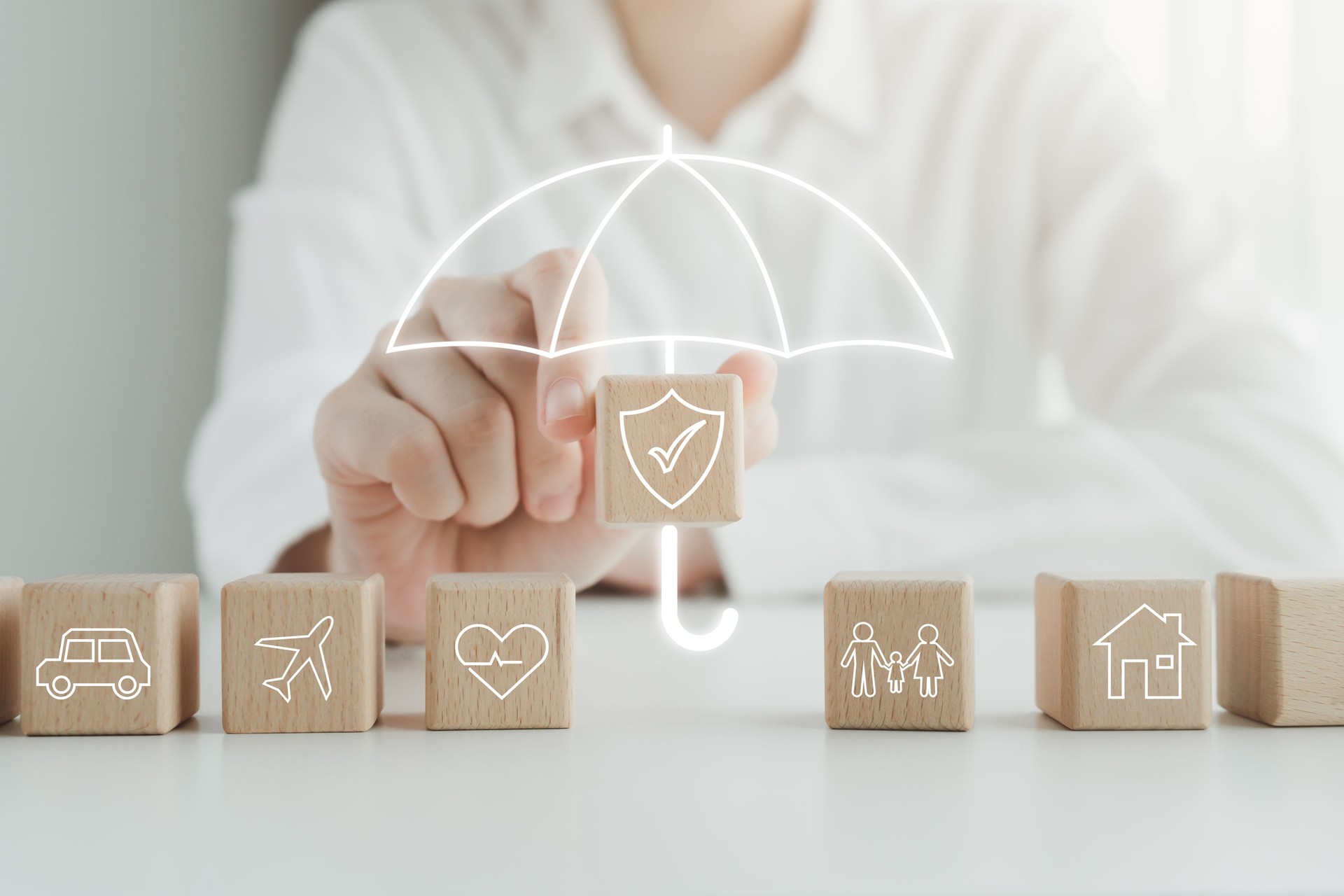Versicherungskonzept. Schutz vor einer möglichen Eventualität. Haus, Auto, Familie, Reisen und Gesundheit auf Holzblock und Hand haltende Sicherheitssymbolabdeckung von Regenschirmsymbol für Lebensversicherungskonzept.